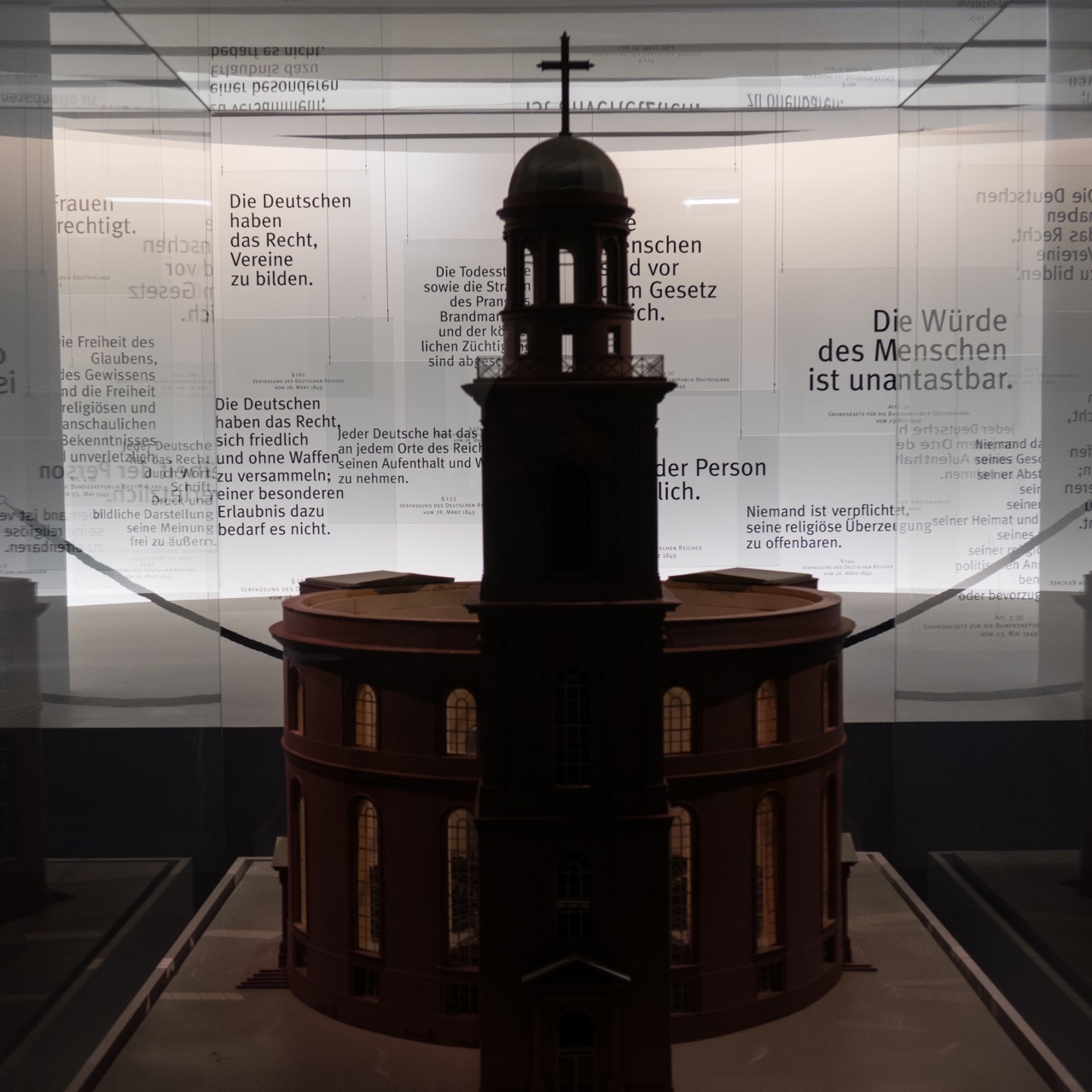 Zitate aus dem Grundgesetz der Bundesrepublik Deutschland, davor ein Modell der Frankfurter <a href="https://www.visit-a-church.info/sacred-buildings/vac/churchbyid.html?id=1513994408445" target="_blank">Paulskirche</a>
